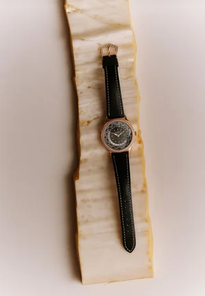 Luxury wristwatch with black leather strap on a vertical ridged marble slab against a plain white background.
