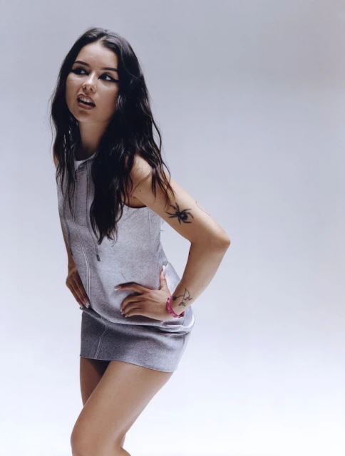 Portrait of a young adult woman posing in a silver dress against a light grey backdrop in a studio. Hands on hips.