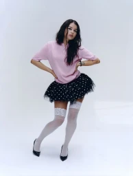 Young woman in a pink polo shirt and black tulle skirt posing against a clean white backdrop