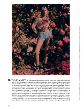 A woman poses in a garden wearing light-colored knitwear and blue shorts, surrounded by pink flowers, captured with a soft, diffused light.