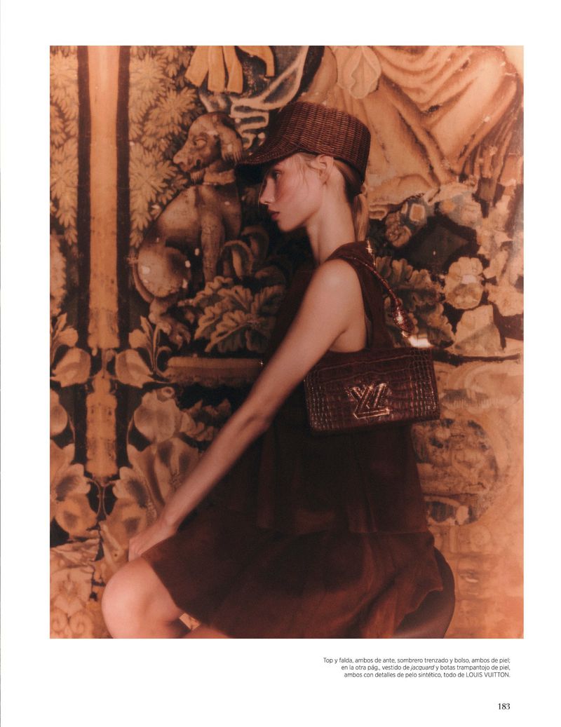 Fashion shoot with a woman in brown dress and cap, accessorized with a Louis Vuitton bag, posing against a decorative tapestry backdrop.