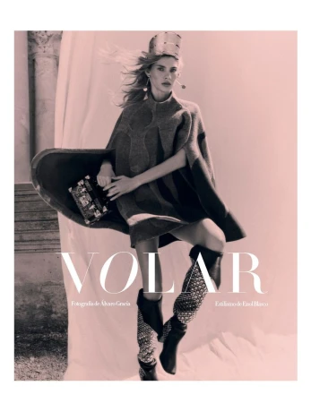 Model in patterned poncho and tall boots holding a small handbag for Harper's Bazaar Espana VOLAR project