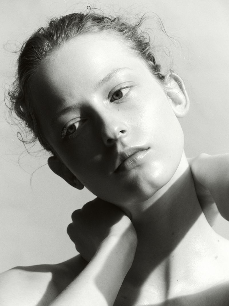 Close-up portrait of a woman with her hand behind her neck against a plain white studio background.