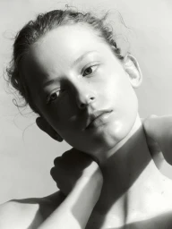 Close-up portrait of a woman with her hand behind her neck against a plain white studio background.
