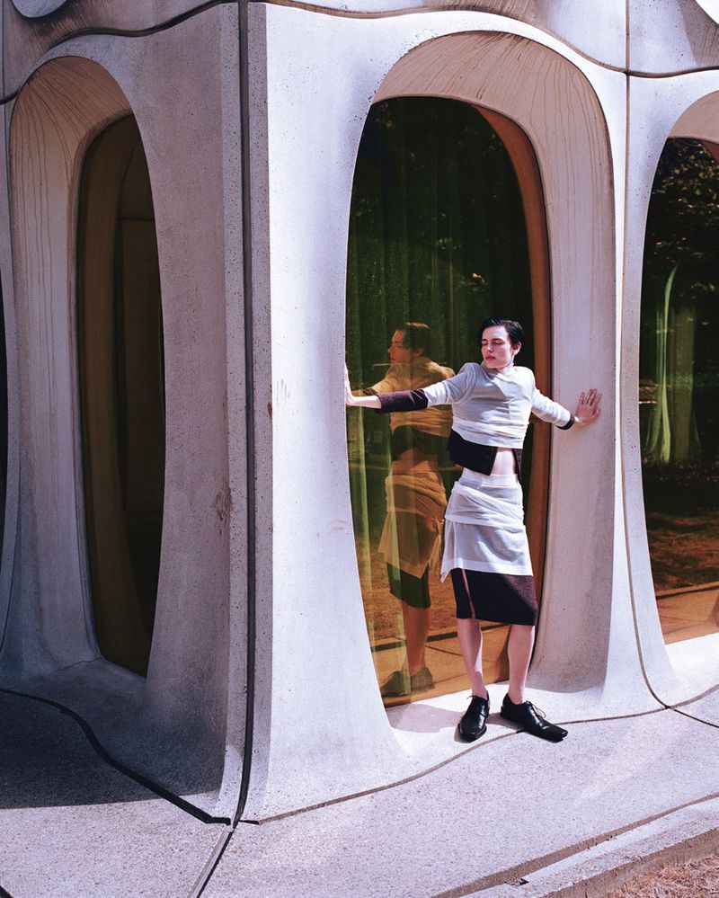 Fashion shot of an adult female posing in front of a building with unique arches, wearing a striped sweater and a black and white skirt.