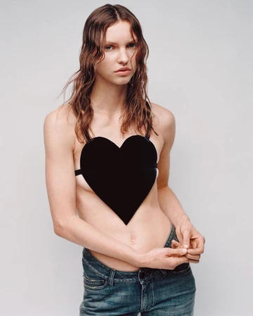 Model wearing a black heart-shaped top and low-rise blue denim jeans against a plain studio background.