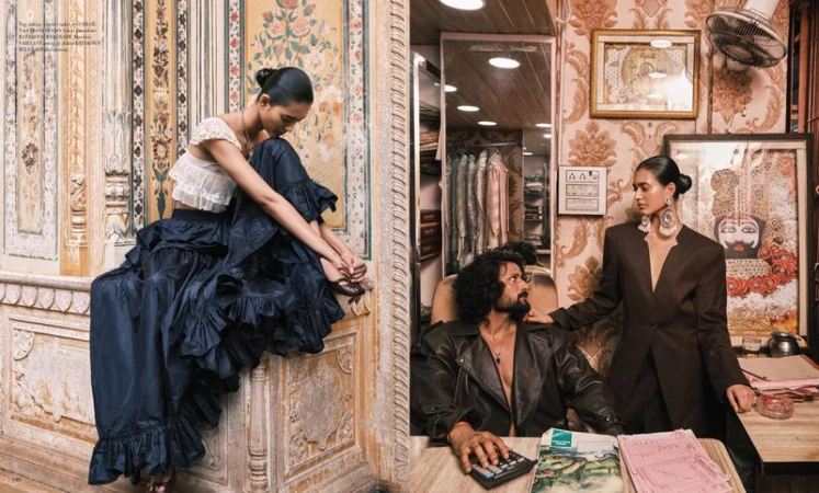 Editorial fashion shot of two women in formalwear with a man in a leather jacket seated behind a counter inside a patterned building.
