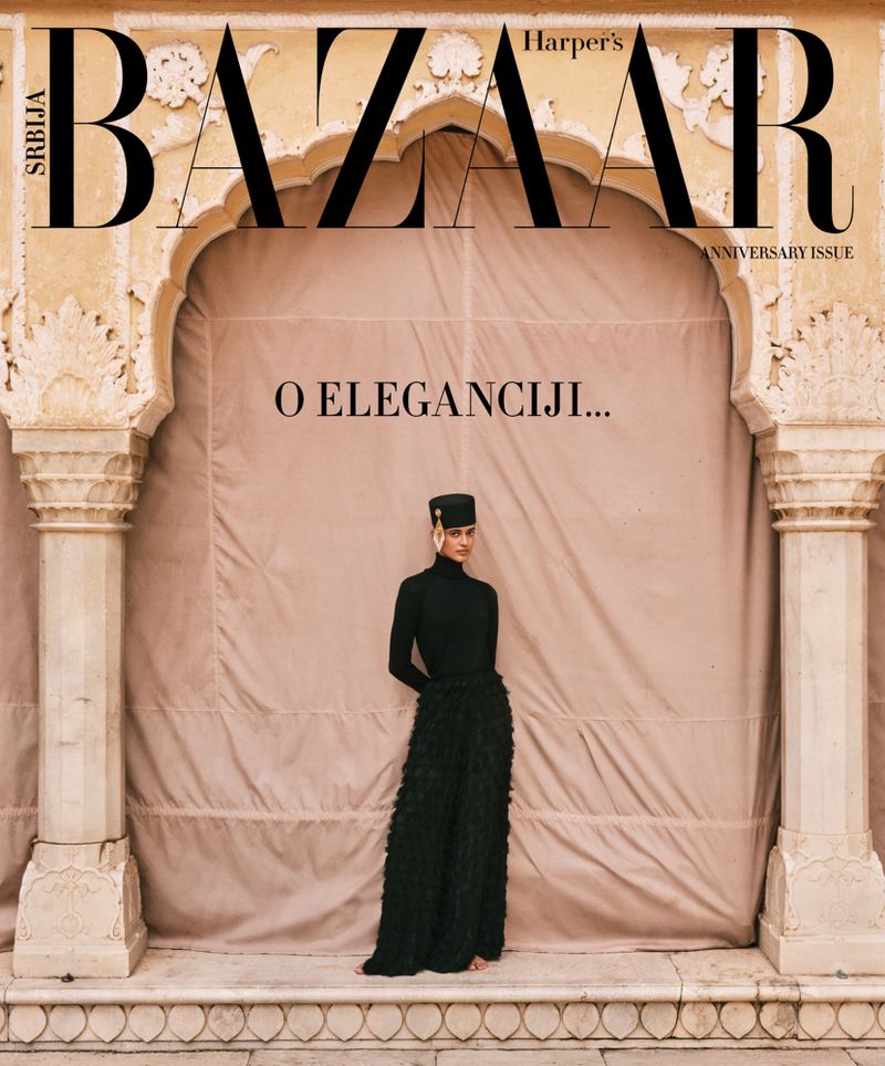 Fashion magazine cover featuring a model in a black outfit and hat, posing in front of an arched doorway with stone pillars.
