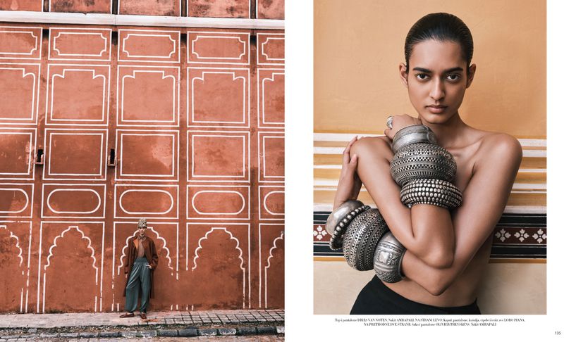 Fashion editorial shot of a woman with bare shoulders wearing bracelets on her upper arms, standing against an orange wall.