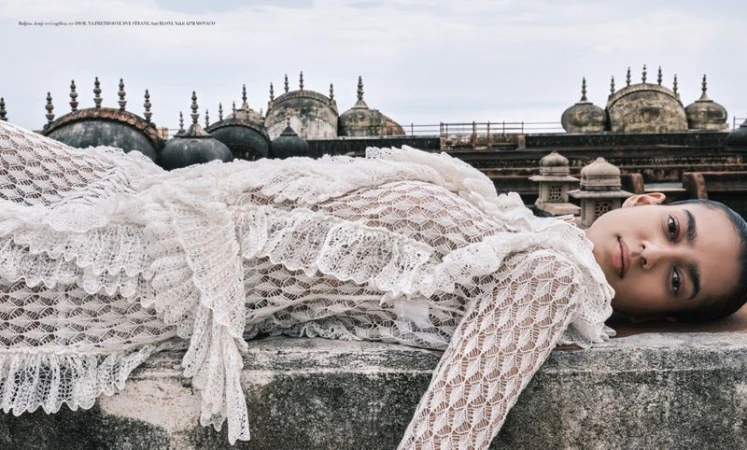 A model in a white lace dress poses on a rooftop with old domes in the background, photographed from a low angle on an overcast day.