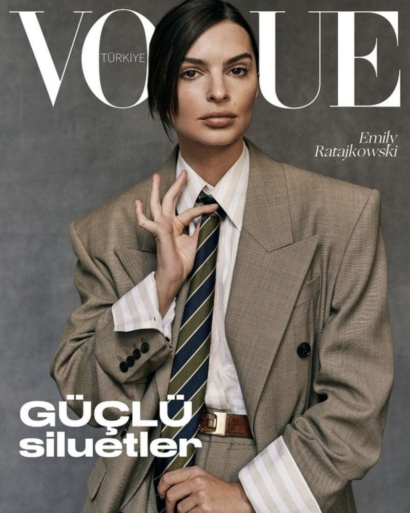 Vogue Turkey cover featuring Emily Ratajkowski in an oversized grey-brown suit, white shirt, and striped tie against a grey backdrop.