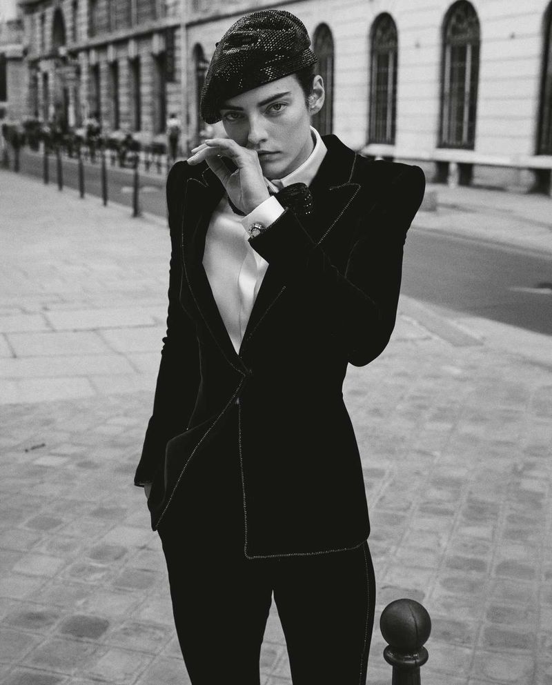 Black and white fashion portrait of an adult woman with a black beret, wearing a suit with strong shoulder pads, on a city street.