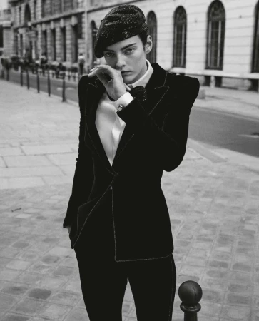Black and white fashion portrait of an adult woman with a black beret, wearing a suit with strong shoulder pads, on a city street.