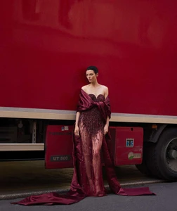 Model in strapless sequined burgundy dress standing against a large red truck for Telegraph Luxury