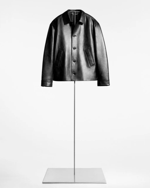 Studio shot of a black leather jacket on a silver stand against a white backdrop, showcasing its design and material.