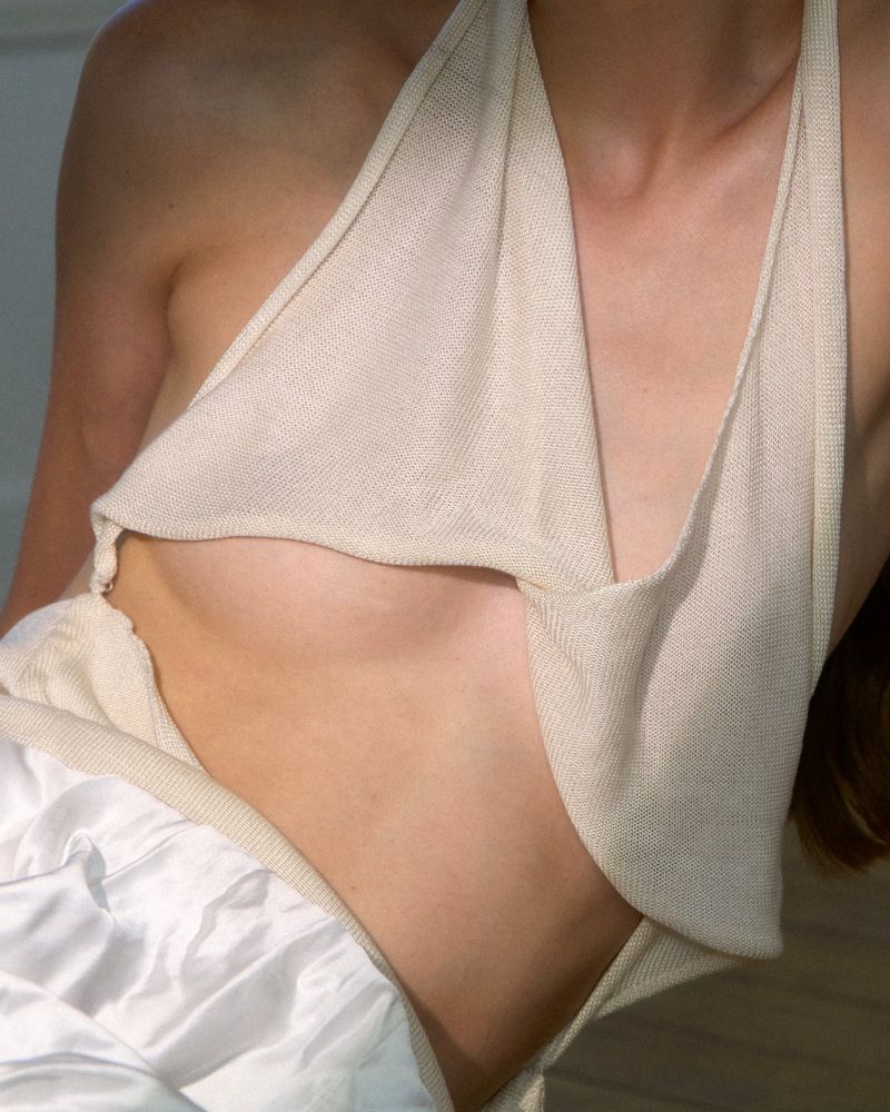 Close-up of a woman wearing a halter top, showcasing the neckline and chest, with a white background and soft, diffused lighting.