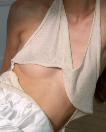 Close-up of a model wearing a draped cream knit halter top and white satin fabric in a studio fashion editorial.