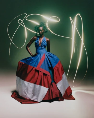 A woman in a colorful dress poses in a studio with light trails. She wears an elegant blue, red, and white gown in a fashion shot.
