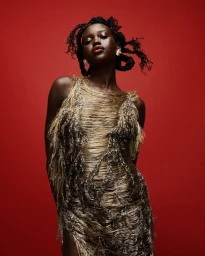 Black woman wearing a shimmering gold fringed dress against a solid deep red background for Vogue Australia A Plus project.