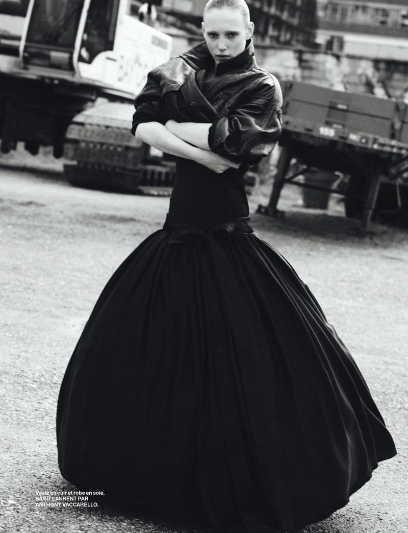 Fashion photo of a slender woman in a voluminous black ballgown, wearing a leather jacket, standing outdoors near construction equipment.