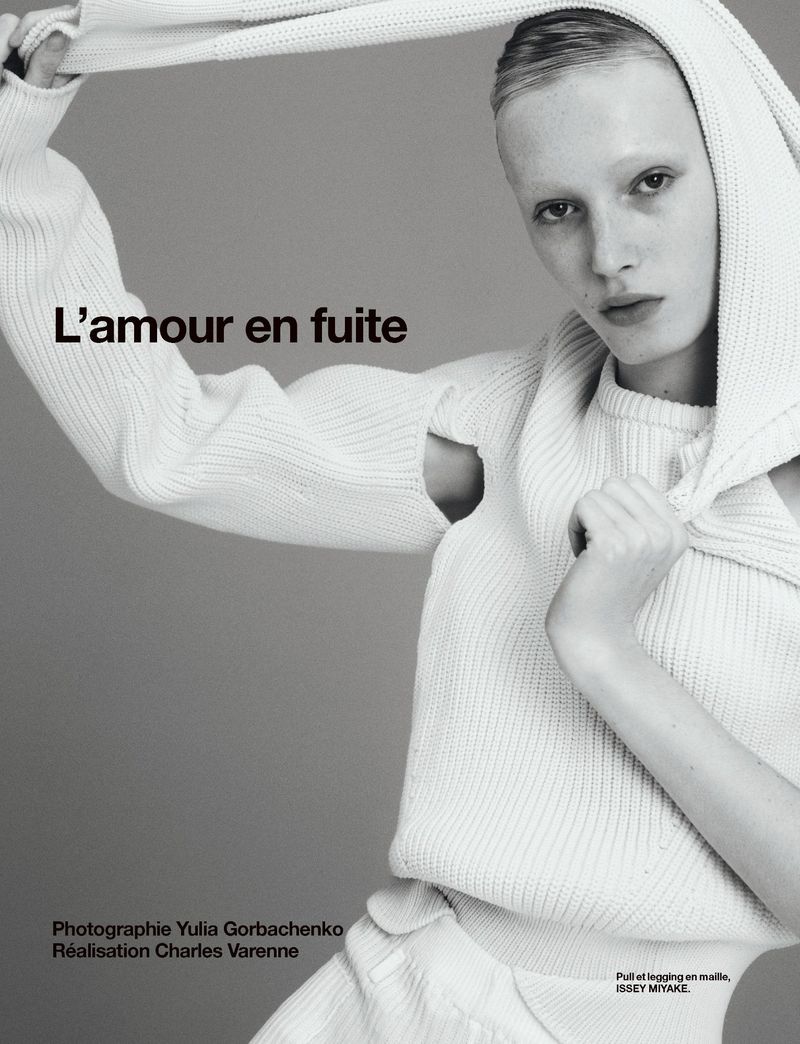 Fashion editorial shot of a model wearing a white knit sweater and hood against a grey background, featuring text overlay and studio lighting.