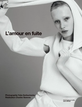 Fashion editorial shot of a model wearing a white knit sweater and hood against a grey background, featuring text overlay and studio lighting.