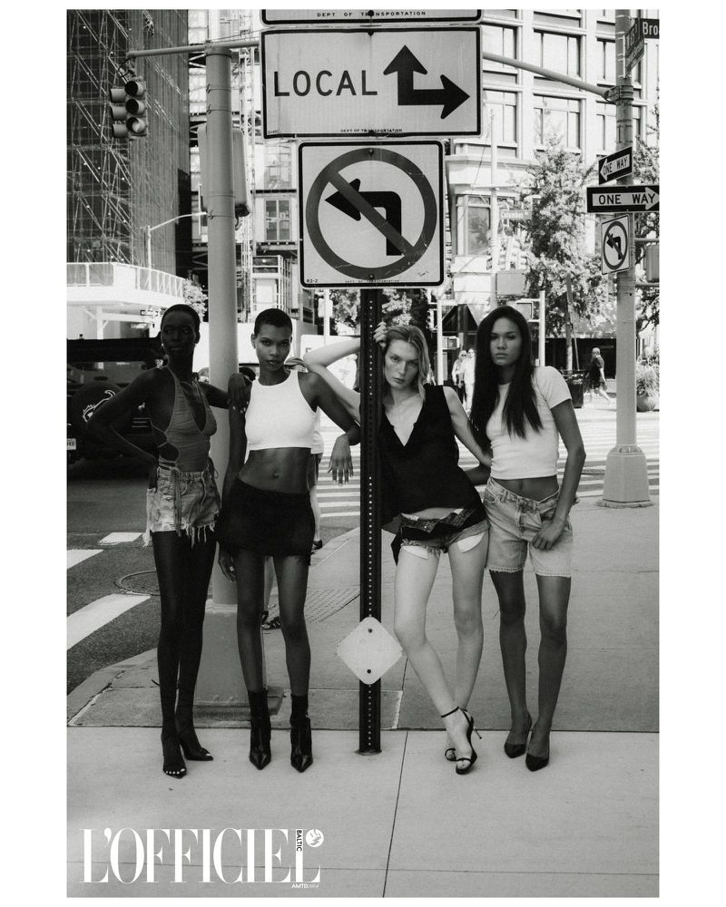 Four women pose in front of street signs wearing casual tops and skirts or shorts in black and white. L'Officiel logo is visible.