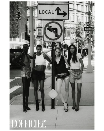 Four women pose in front of street signs wearing casual tops and skirts or shorts in black and white. L'Officiel logo is visible.