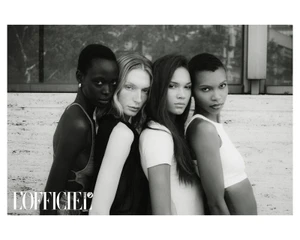 Black and white editorial portrait of four diverse female models posing together outdoors against a textured architectural stone wall.