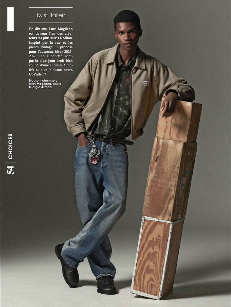 A stylish, dark-skinned male model poses in a collared shirt, jacket, and jeans next to a stack of wooden boxes in a fashion editorial.