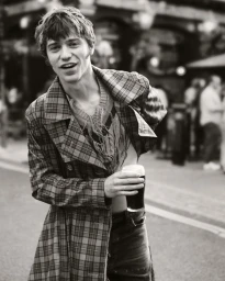Young man wearing a plaid coat holding a pint of stout on an outdoor street