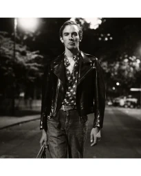 Monochrome portrait of a male model in a leather jacket and star print shirt walking on a street at night.