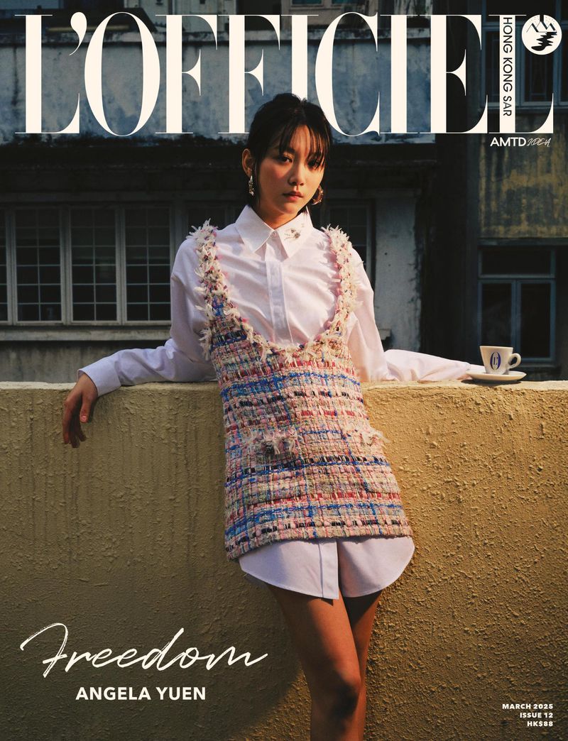 Magazine cover featuring a young woman in a layered outfit of white shirt and tweed vest leaning against a wall outdoors with buildings in the background.