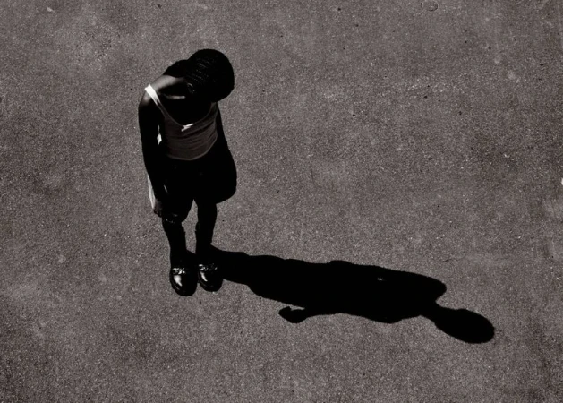 High-angle shot of an African-American woman standing on concrete, casting a shadow, in monochrome. She wears casual clothing.