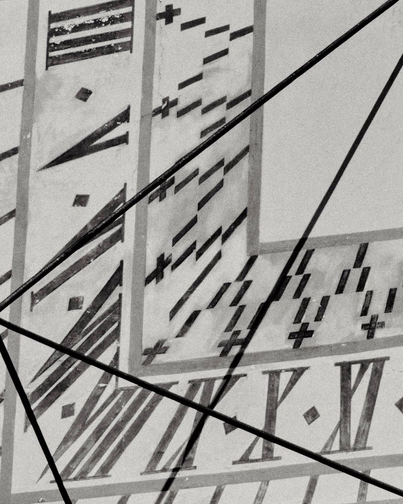 Close-up of an old sundial face, showcasing Roman numeral time markings, linear shadows, and geometric patterns, creating a vintage aesthetic.