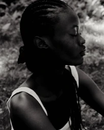 Black and white portrait of a black woman in profile with braided hair wearing a white tank top outdoors.