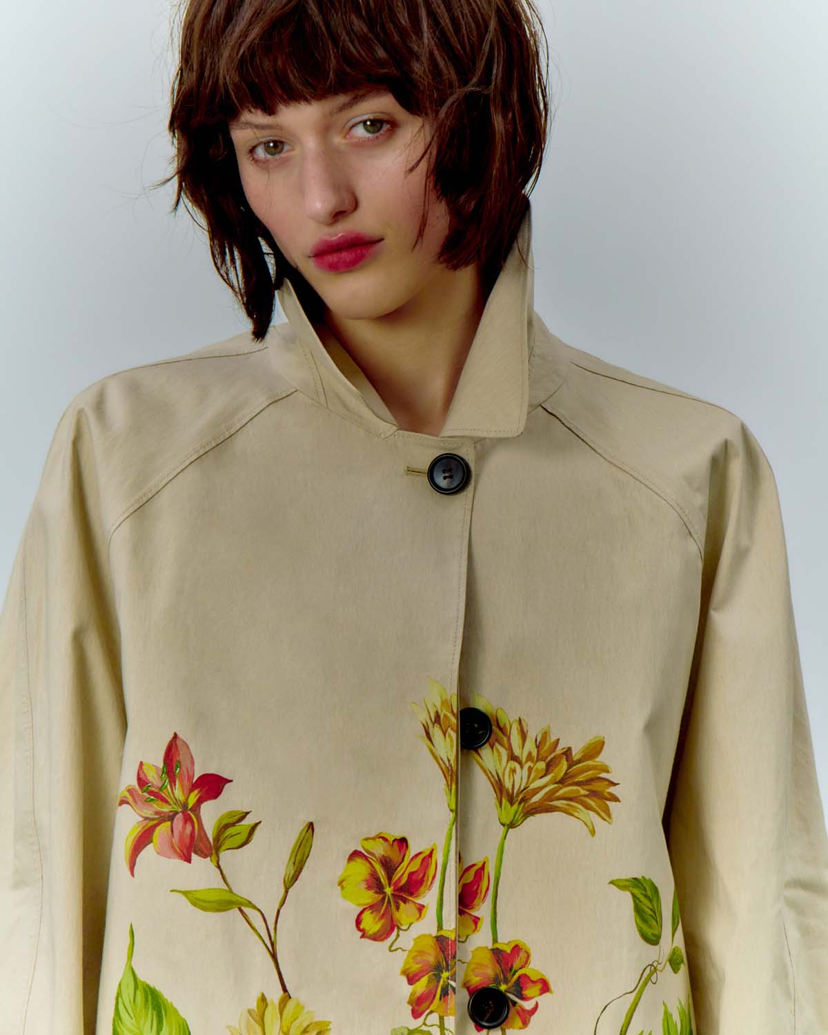 Portrait of a woman wearing a beige button-down coat with floral print details for COAT Magazine