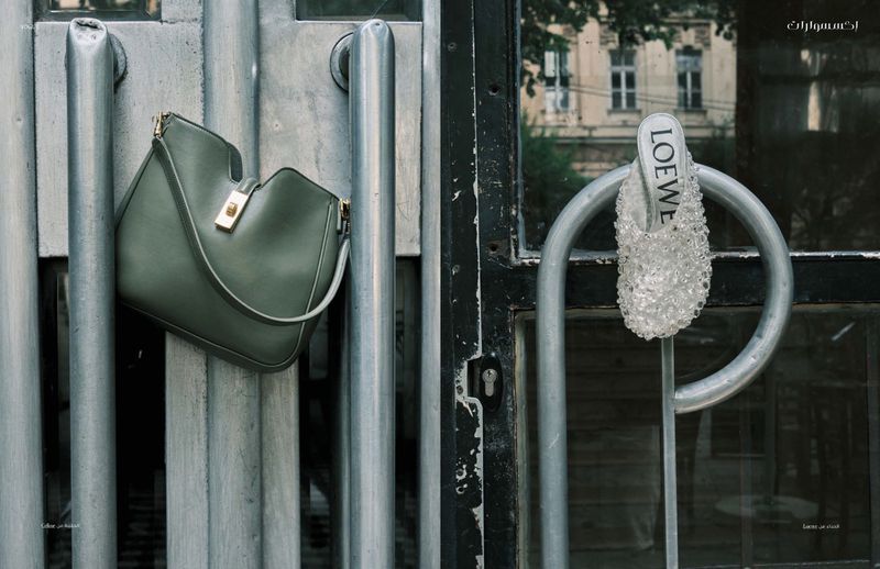 Loewe handbag in olive green hanging on metal door bars with a Loewe beaded shoe on the opposite side, urban setting, neutral tones.