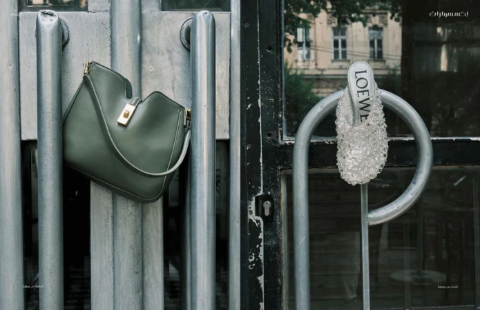 Loewe handbag in olive green hanging on metal door bars with a Loewe beaded shoe on the opposite side, urban setting, neutral tones.