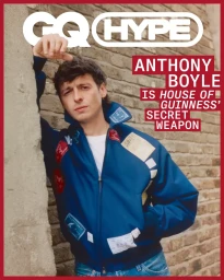 Actor Anthony Boyle leaning against a brick wall wearing a blue jacket over a white t-shirt for British GQ.