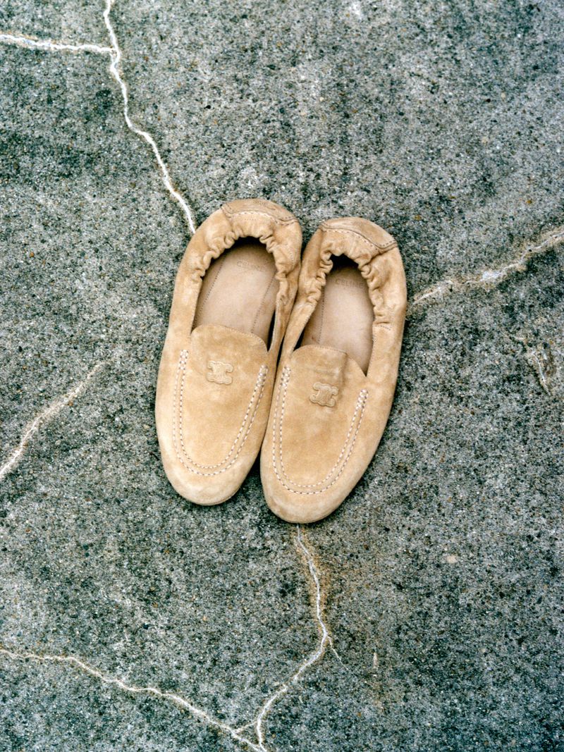 Overhead shot of tan suede slip-on shoes on a cracked concrete surface, showcasing the material and texture of the footwear.