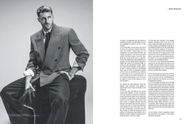 Santi Gimenez seated in a tailored double-breasted blazer and tie for a monochrome magazine editorial feature.