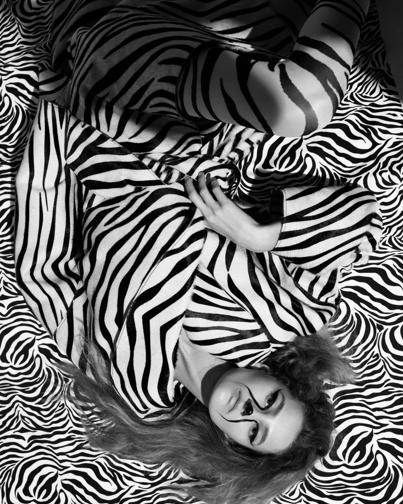Woman in zebra-striped outfit lying on matching patterned fabric, showcasing a bold black and white aesthetic with striking makeup.