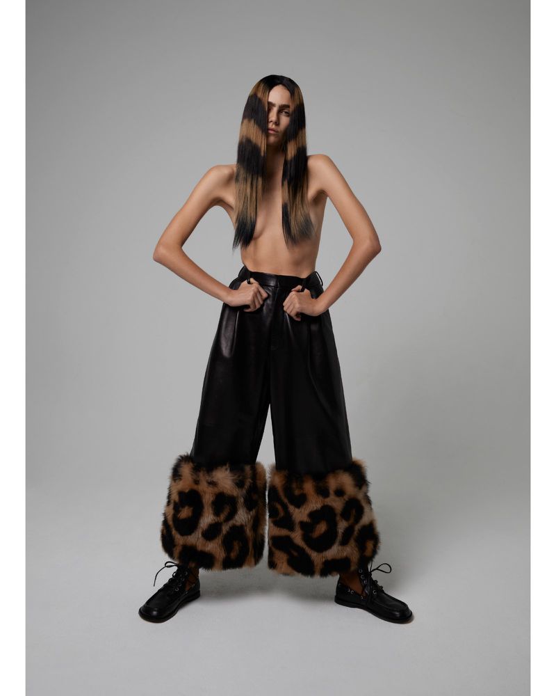Fashion portrait of a woman with blond and black hair extensions, black leather pants with leopard print cuffs, and black shoes in studio.
