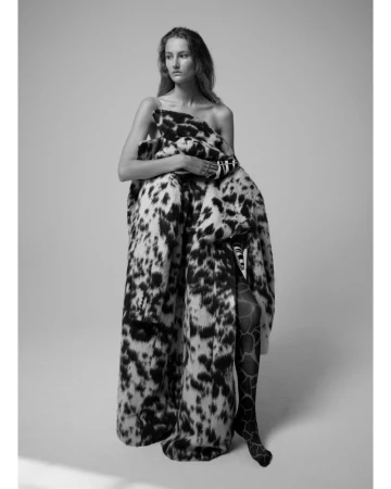 Model wrapped in a patterned black and white coat against a plain studio background