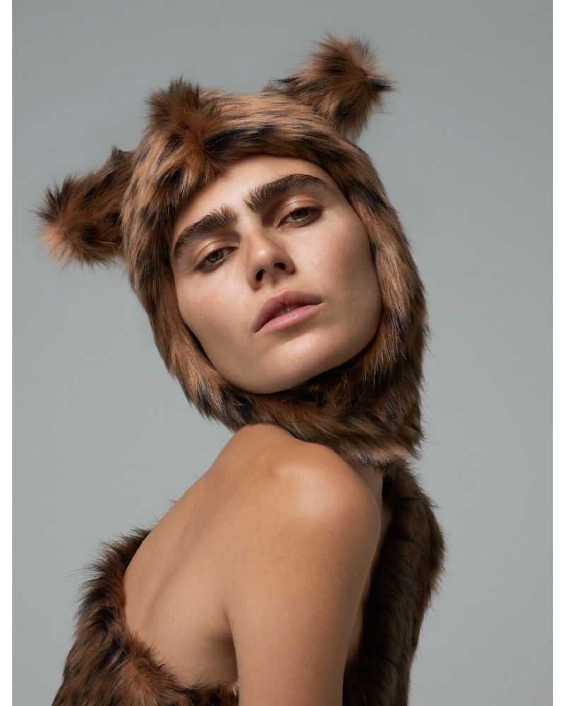 Woman wearing a fur-like animal-eared hood in a studio setting. The image features a close-up studio shot with diffused lighting.