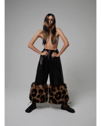 Model with striped hair wearing black leather trousers with faux fur cuffs against a grey background