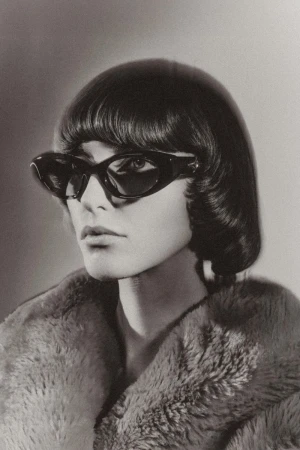 Model wearing dark sunglasses and a textured fur coat with a short bob haircut against a gradient background.