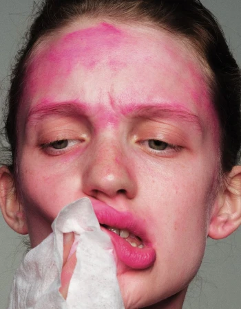 Close-up of a woman with pink makeup removing makeup with a tissue. Beauty shot focusing on makeup and skincare in a minimal setting.
