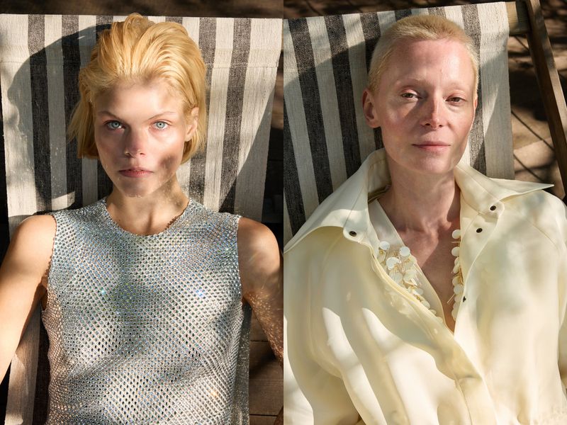 Two women with short blond hair pose in a close up shot, one wearing a shiny silver top and the other in a sheer, light yellow top.